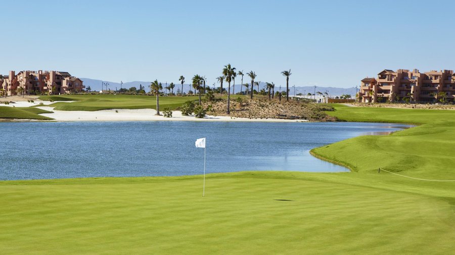 Golf green beside a lake, with palms and apartments beyond